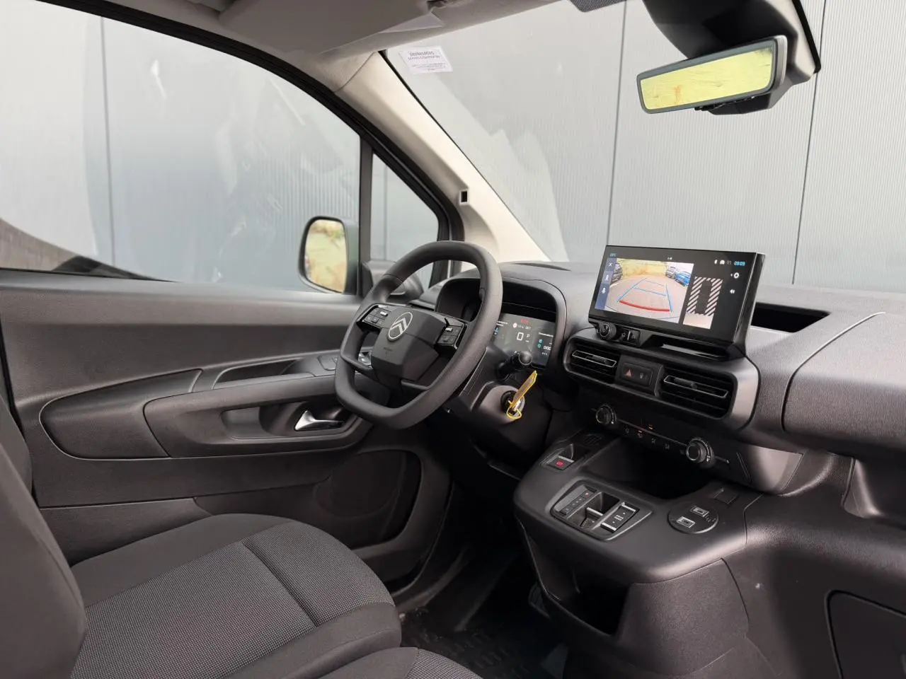 Vue intérieure côté conducteur du Citroën Berlingo blanc, avec tableau de bord numérique et écran tactile affichant la caméra de recul.
