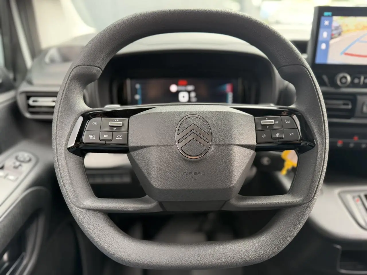 Vue rapprochée du volant multifonctions noir du Citroën Berlingo 2026, avec tableau de bord numérique et écran tactile visible.