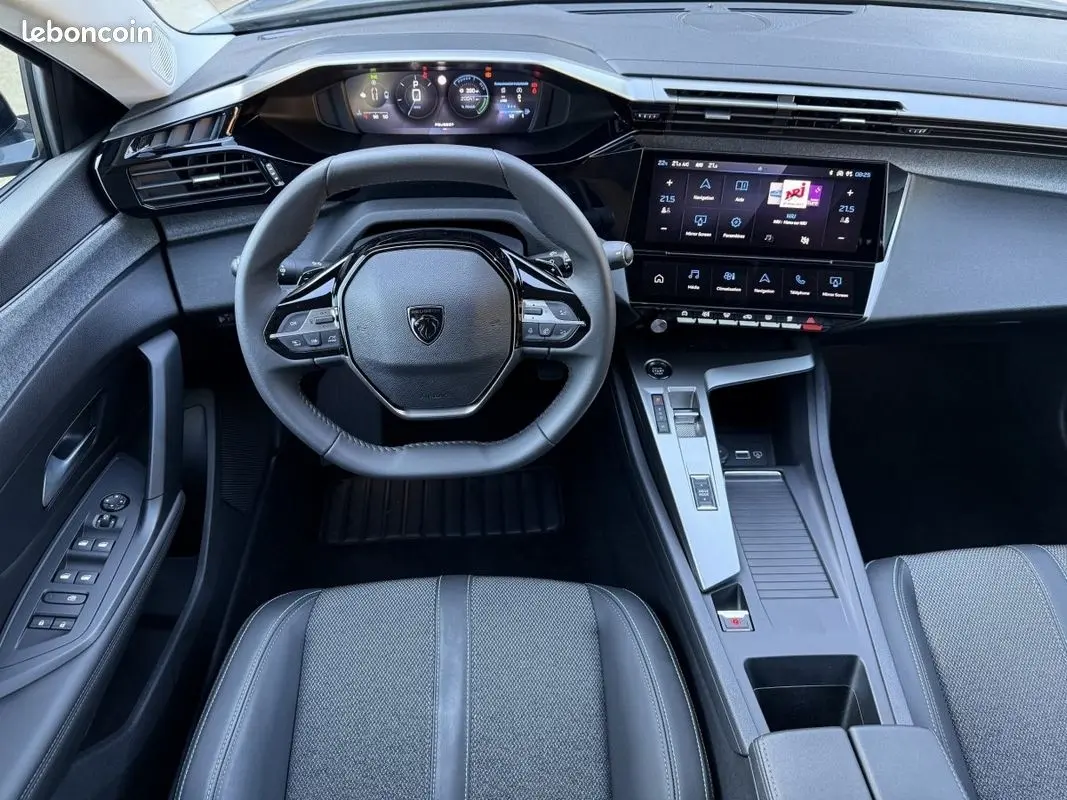 Vue intérieure avant de la Peugeot 308 Hybrid 145 e-DCS6 Allure 2025, tableau de bord et volant cuir noir.