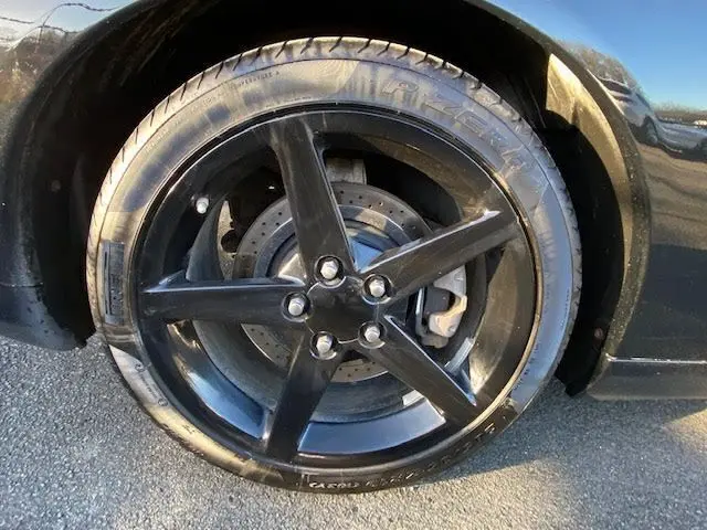 Gros plan sur la roue avant gauche noire d'une Chevrolet Corvette C6 Targa 2005, jante cinq branches et disque ventilé visible.