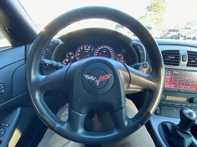 Vue intérieure centrée sur le volant noir de la Chevrolet Corvette C6 Targa 2005 avec tableau de bord et levier de vitesse manuel visible.
