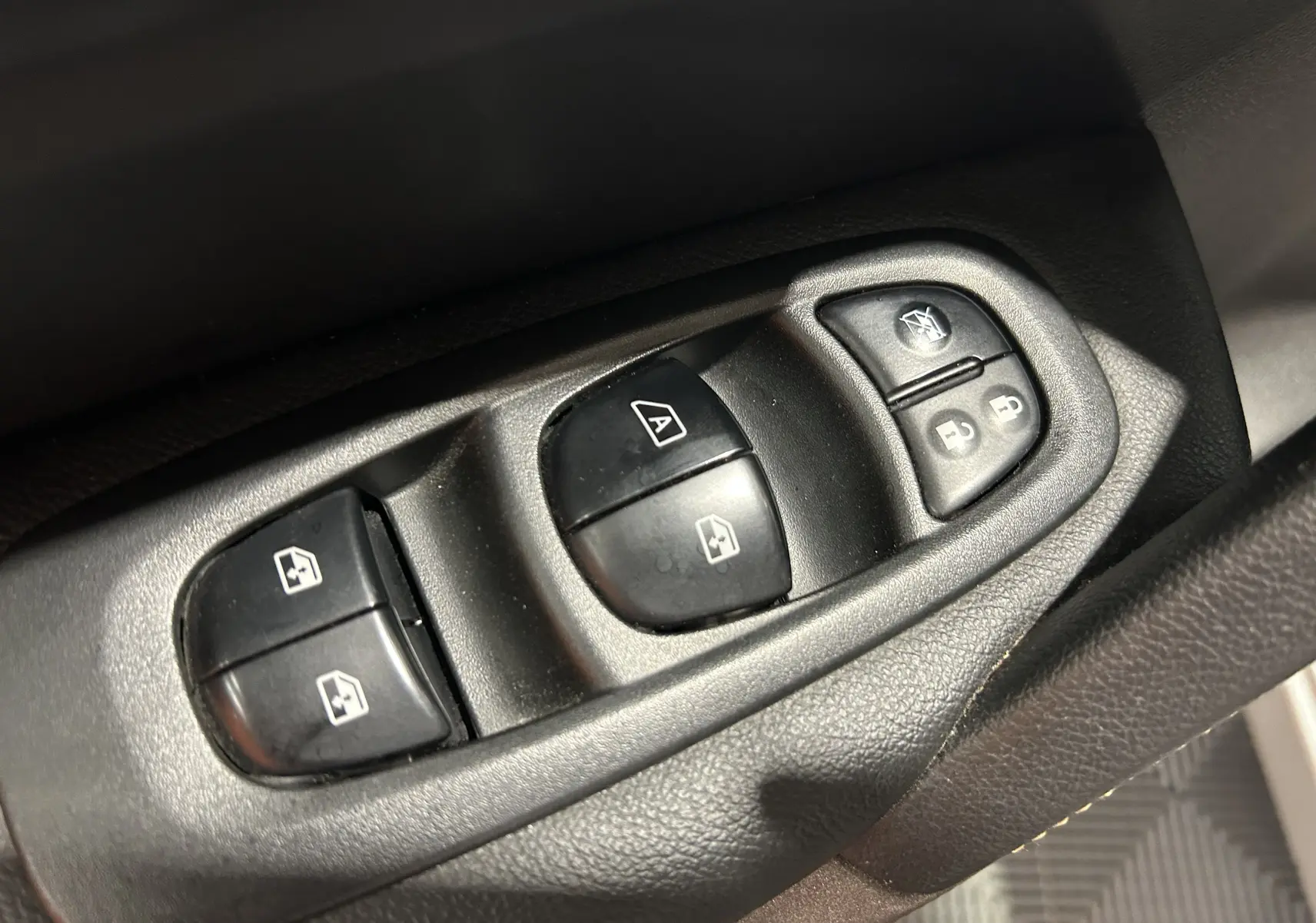 Gros plan sur les commandes de lève-vitres et verrouillage des portes côté conducteur d'un Renault Kadjar gris 2015.