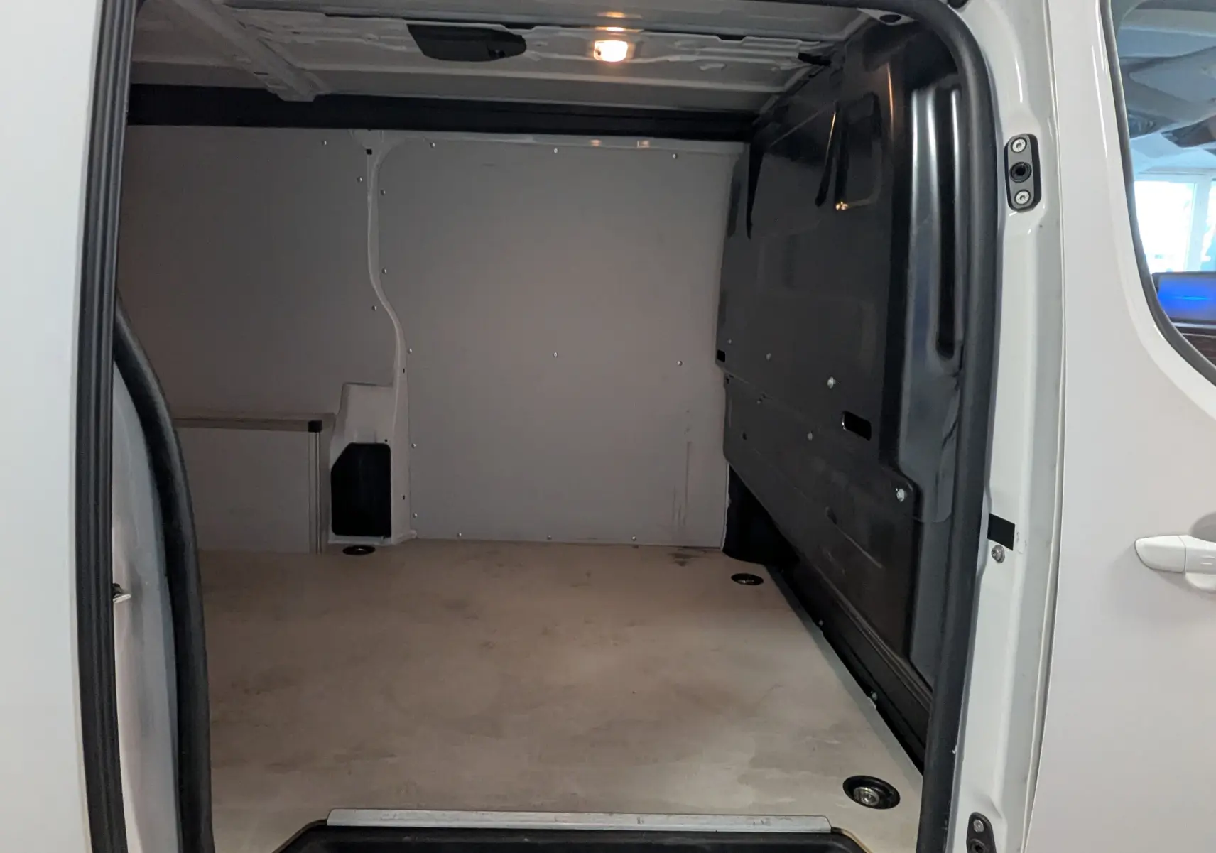 Vue intérieure du compartiment de chargement du fourgon Opel Vivaro XL blanc, avec plancher et parois protégés en bois.