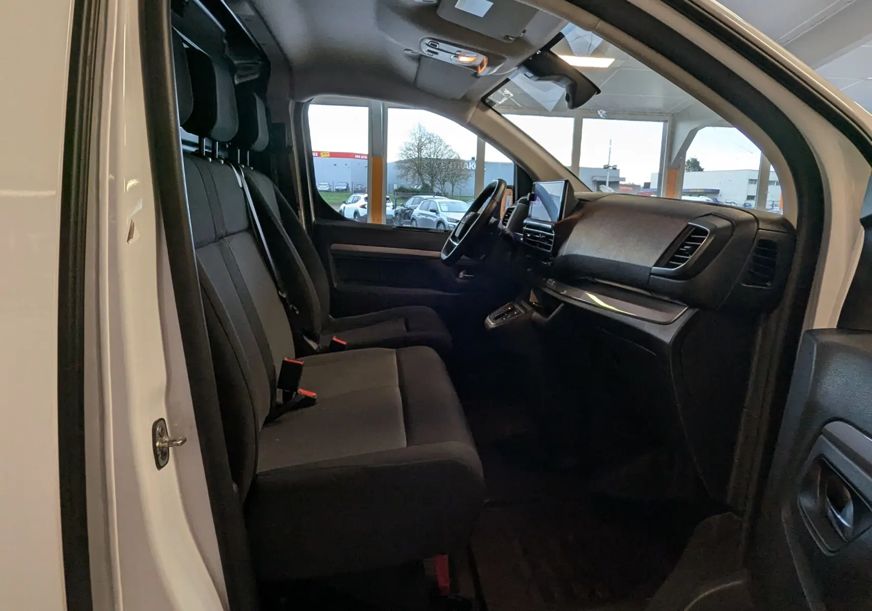 Vue intérieure côté conducteur de l'Opel Vivaro Fourgon blanc 2024, montrant les sièges noirs et le tableau de bord moderne.