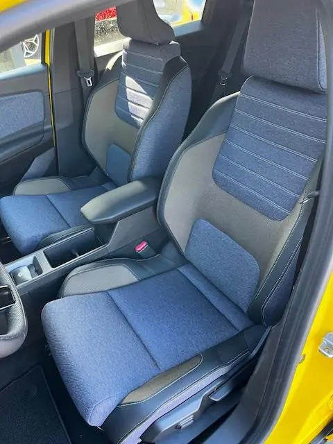 Vue intérieure côté avant droit de la Renault R5 Techno 150 ch 2024 jaune, sièges tissu bleu et gris avec accoudoir central.