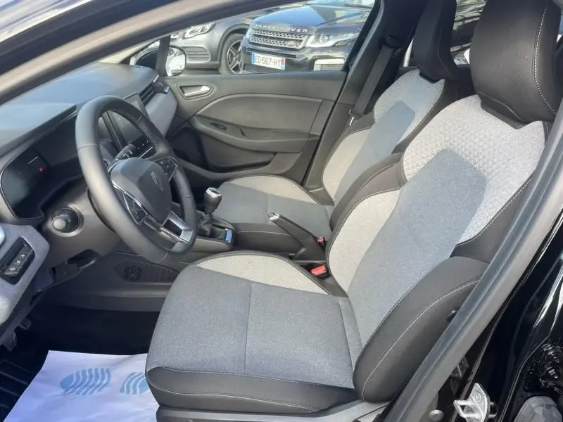 Intérieur avant droit de la Renault Clio V 1.5 DCI 100 Evolution 2025 noire, sièges tissu gris et volant multifonction.