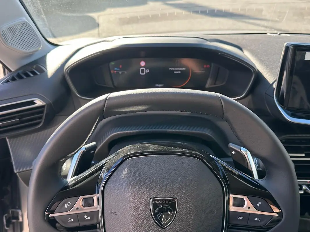 Vue rapprochée du volant cuir noir Peugeot 208 Hybrid 2025 avec commandes intégrées et tableau de bord numérique.