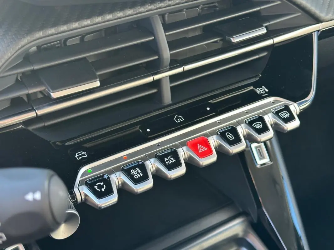 Gros plan sur la console centrale de la Peugeot 208 gris 2025, montrant les commandes tactiles et boutons métalliques.