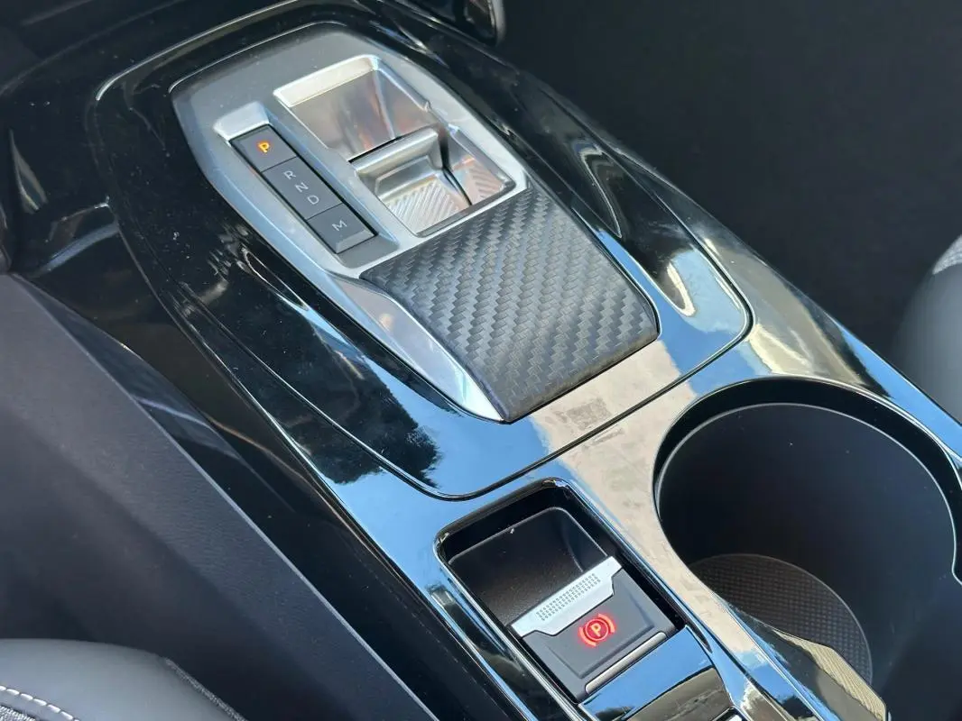 Gros plan sur la console centrale noire brillante de la Peugeot 208 Hybrid 110, avec levier de boîte auto et frein à main électrique.
