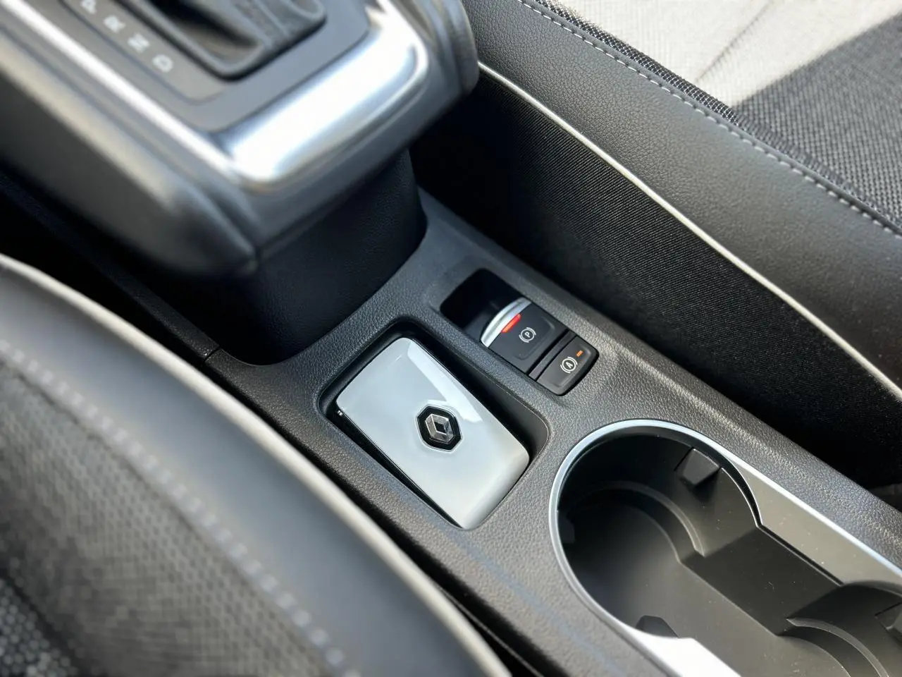 Gros plan sur la console centrale noire avec bouton de frein à main électrique et porte-clés Renault gris brillant.