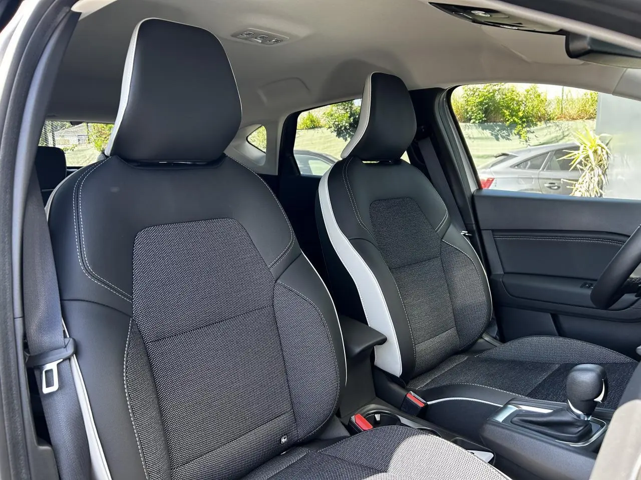 Vue intérieure avant du Renault Captur 2024, sièges bi-matière noirs et gris avec surpiqûres blanches.