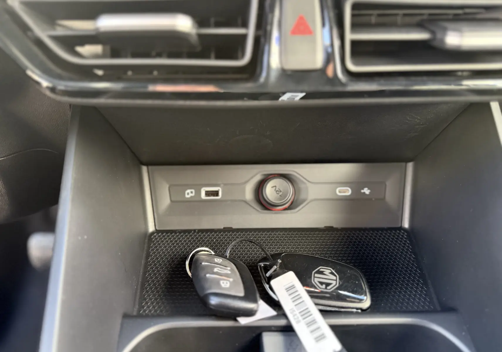 Gros plan intérieur sur la console centrale noire avec clés MG posées, prise 12V et ports USB visibles.