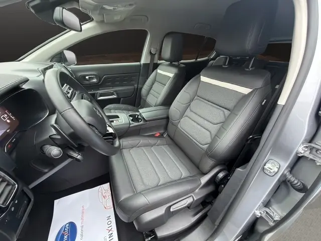 Vue intérieure côté conducteur de la Citroën C5 Hybride gris clair 2024, sièges tissu et cuir avec console centrale visible.