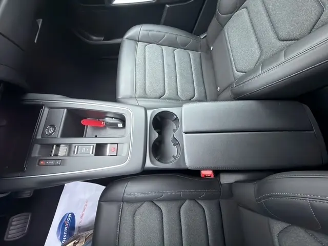 Vue intérieure centrée sur la console centrale et les sièges avant en cuir noir du Citroën C5 hybride 2024.
