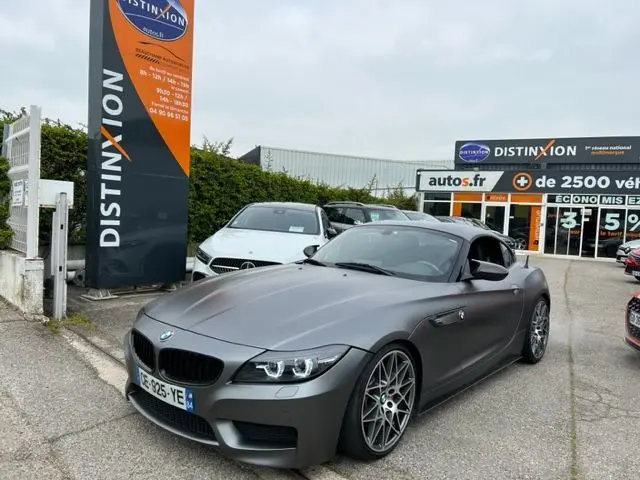 BMW Z4 Roadster grise vue 3/4 avant droit, avec jantes sport et calandre noire, stationnée devant un concessionnaire.