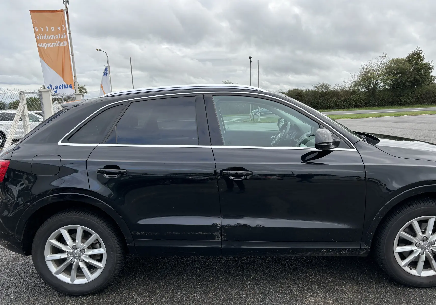 Profil côté gauche d'un Audi Q3 noir de 2014, mettant en valeur ses jantes alliage et ses vitres teintées.