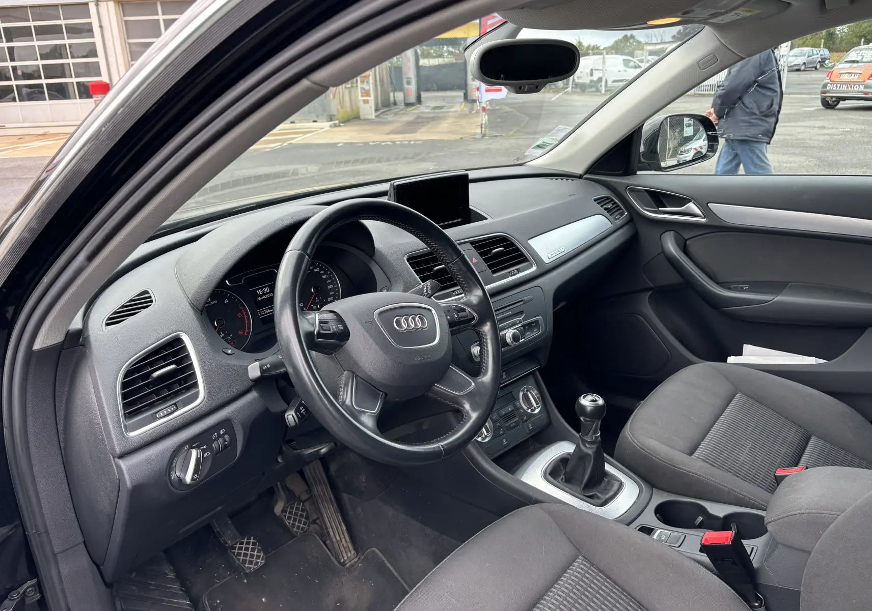 Intérieur noir de l'Audi Q3 2014 vu côté conducteur, avec volant cuir, tableau de bord et levier de vitesse manuel visibles.