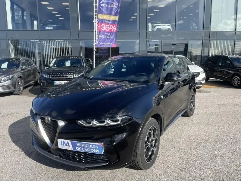 Alfa Romeo Tonale noir vue 3/4 avant droit, avec calandre distinctive et jantes spécifiques, stationné devant un showroom.