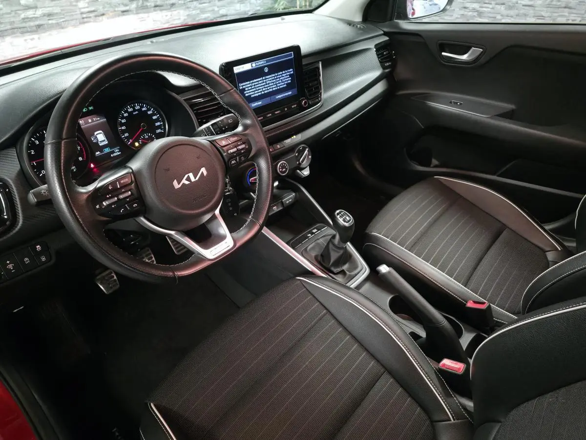 Vue intérieure côté conducteur de la KIA Rio rouge 2022, volant cuir GT Line et console centrale avec écran tactile.