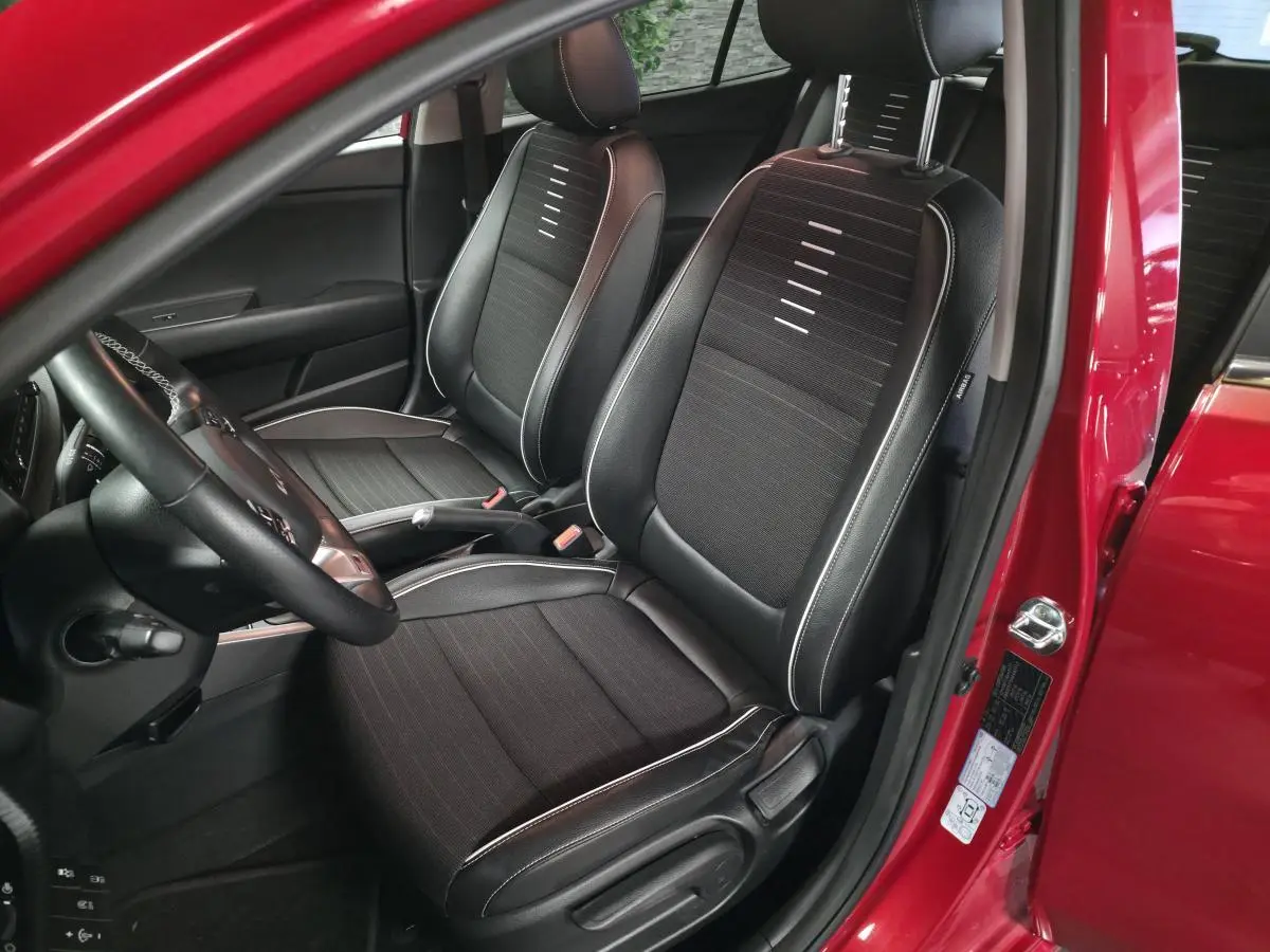 Vue intérieure côté conducteur de la KIA Rio rouge 2022, sièges bi-ton cuir tissu noir avec surpiqûres grises.