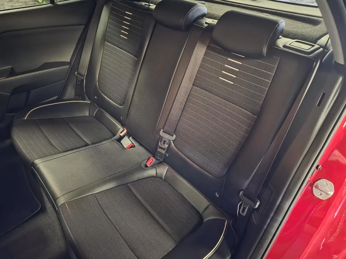 Vue intérieure sur la banquette arrière noire de la KIA RIO rouge, soulignant les ceintures et finitions cuir-tissu.