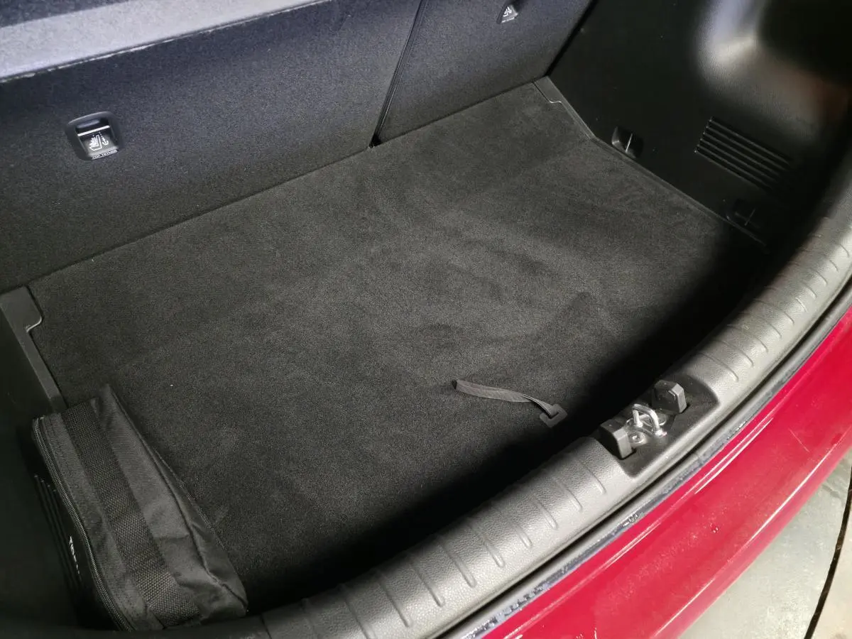 Coffre ouvert vu de dessus d'une KIA RIO rouge 2022, avec tapis noir et bordure de coffre en plastique.