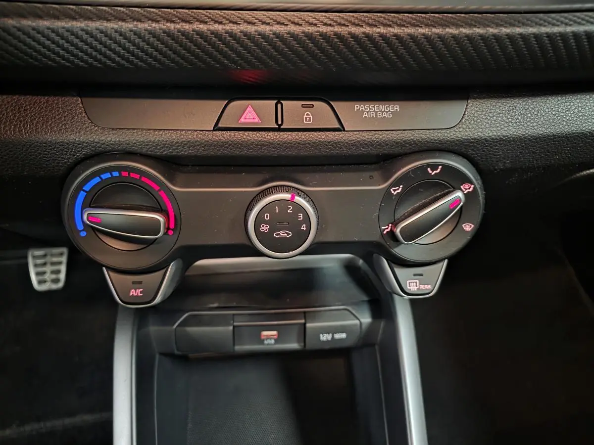 Vue rapprochée de la console centrale de la Kia Rio rouge 2022, montrant les commandes de climatisation manuelle et prises USB/12V.