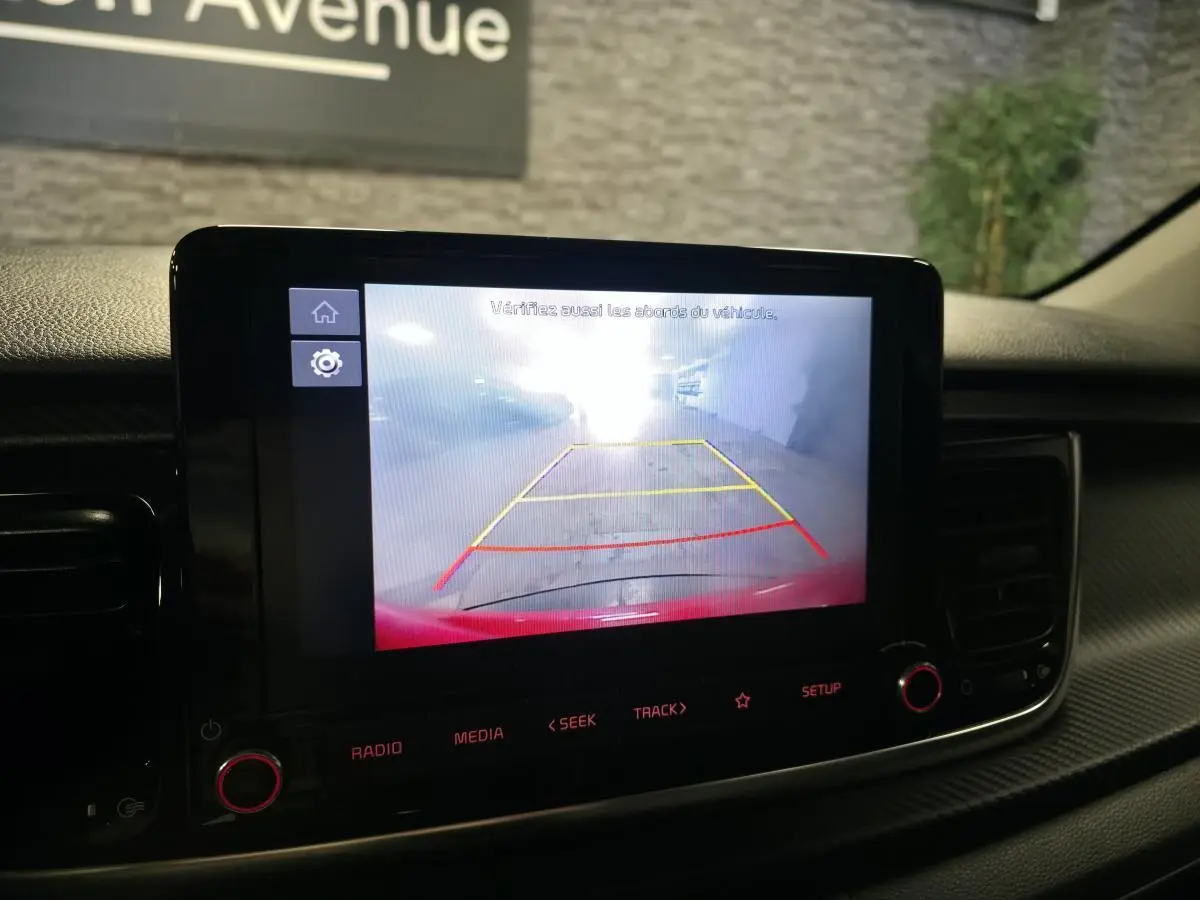 Écran tactile intérieur affichant la caméra de recul d'une Kia Rio rouge, vue du tableau de bord.
