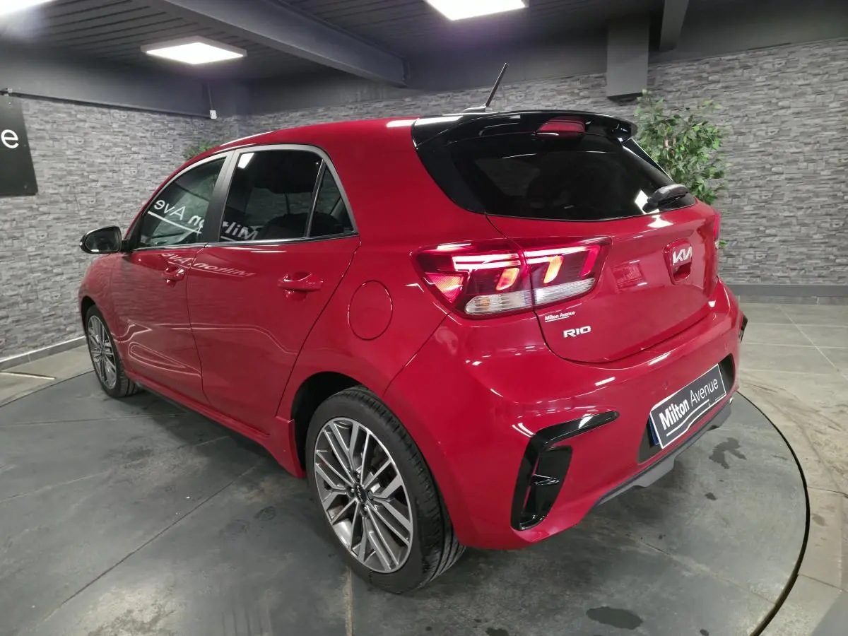 Vue 3/4 arrière droite d'une KIA Rio rouge métallisée GT Line avec jantes alliage et becquet noir laqué.