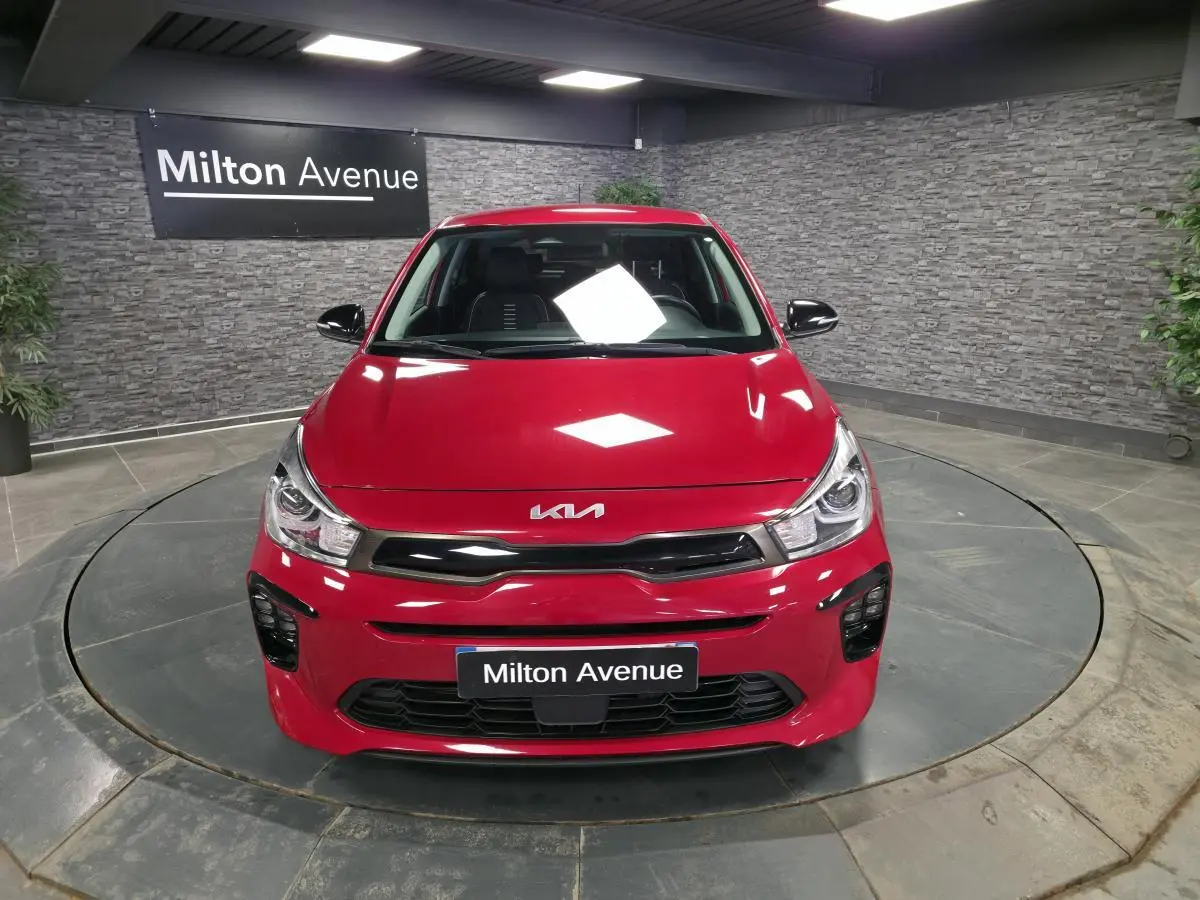 Vue avant d'une KIA Rio rouge métallisée GT Line 2022 avec calandre noire et phares LED dans un showroom.