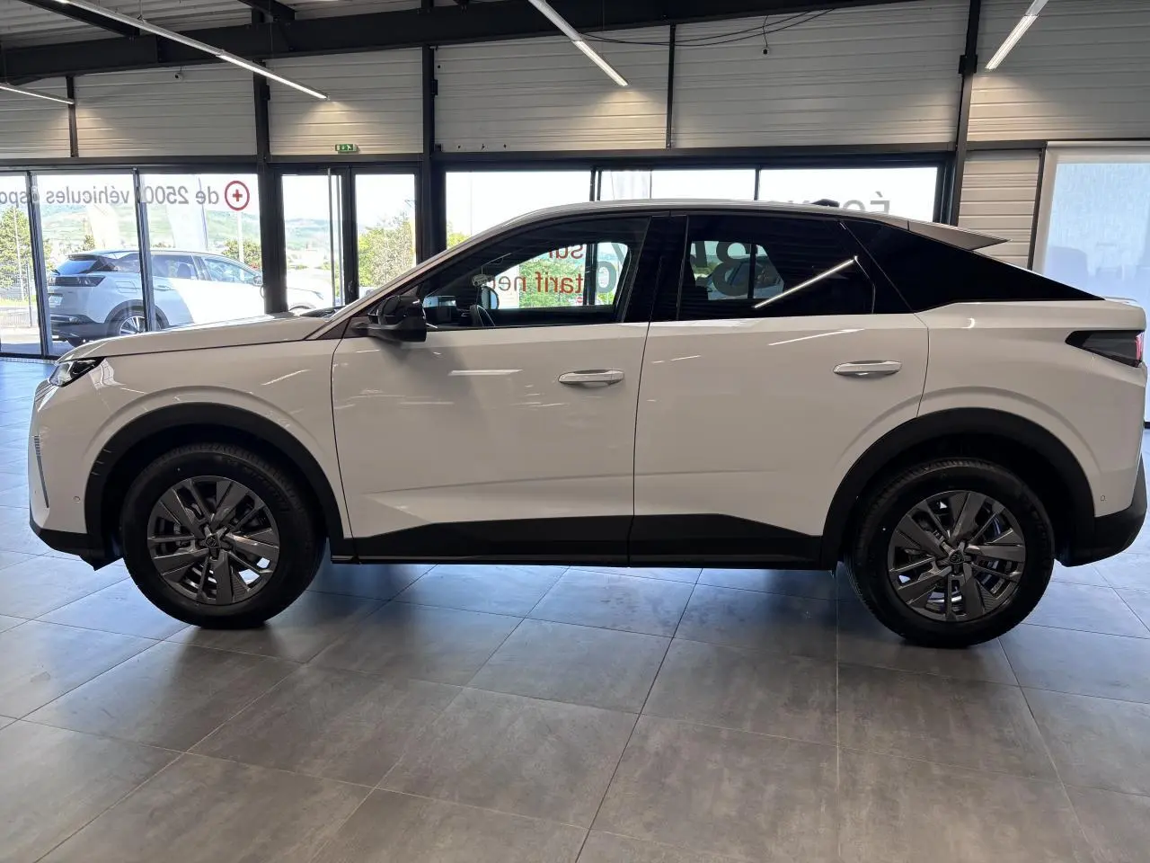 Vue de profil côté gauche d'un Peugeot 3008 blanc avec toit noir et jantes alliage 18 pouces en intérieur de showroom.