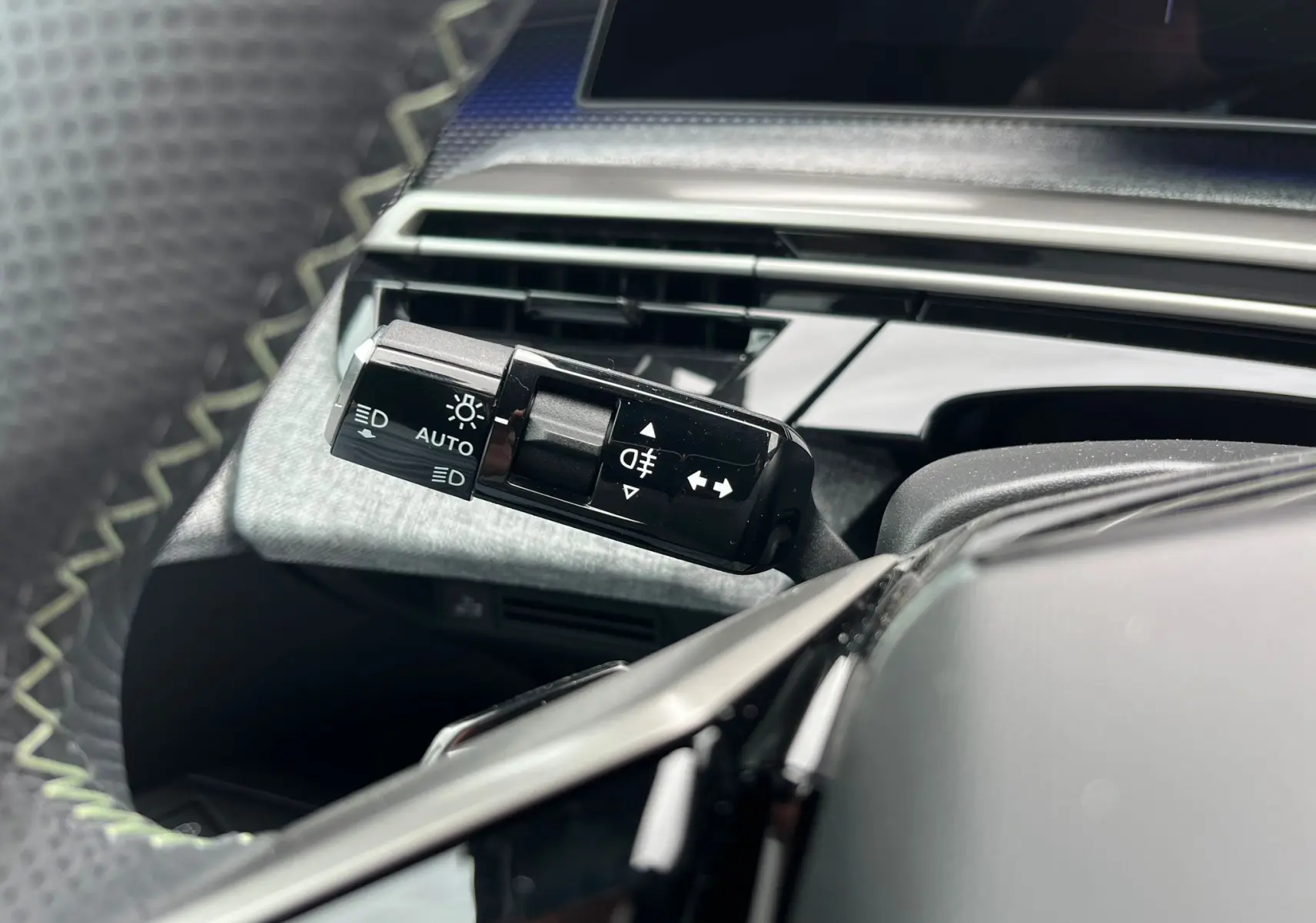 Gros plan sur la commande des feux et clignotants à gauche du volant dans l'habitacle noir du Peugeot 3008 Hybrid 2025.