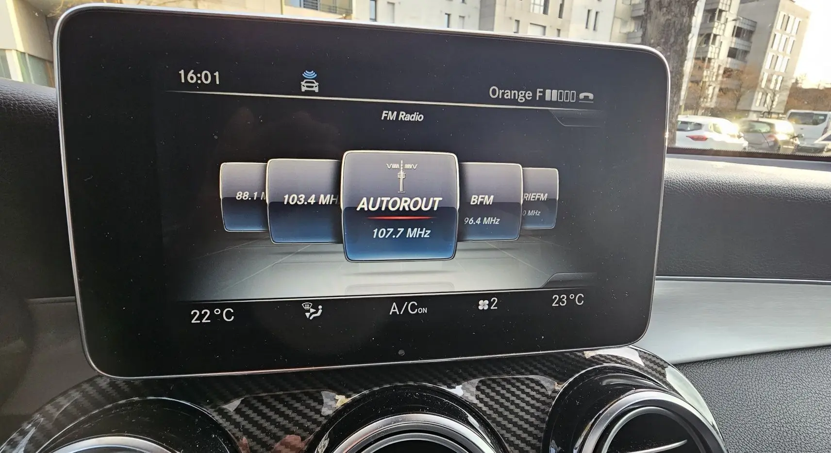 Écran central affichant la radio FM à 107.7 MHz dans le Mercedes GLC 220 Coupé blanc, vue intérieure avant.