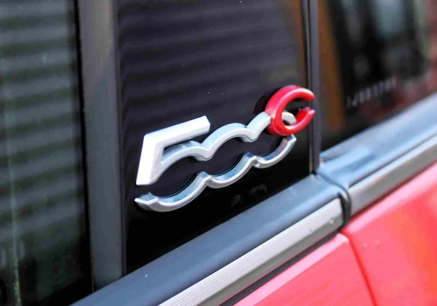 Vue 3/4 arrière droite d'une Fiat 500C 2018 rouge Pastel Coral avec toit ouvrant replié et jantes multibranches.