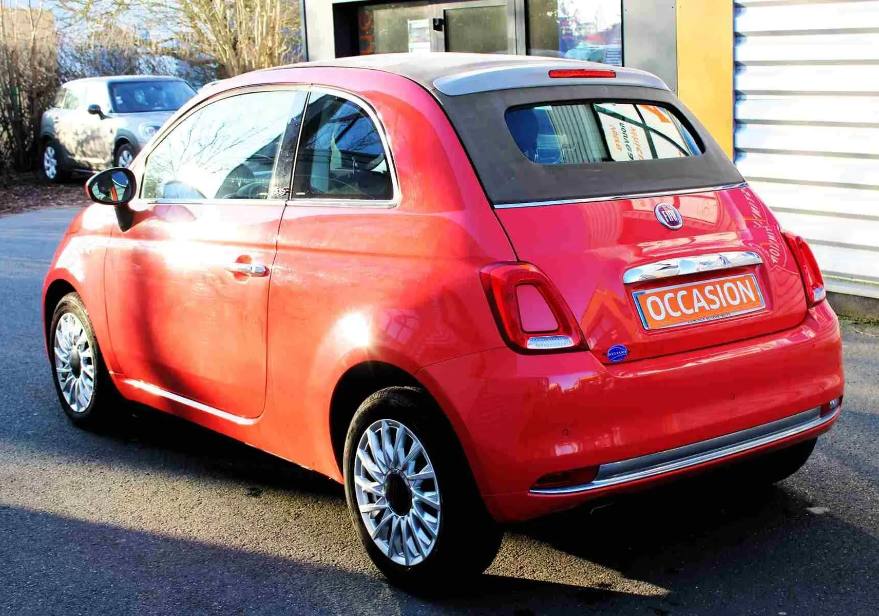 Vue 3/4 avant droite d'une FIAT 500C 2018 rouge Pastel Coral avec plaque "OCCASION" visible sur un parking.