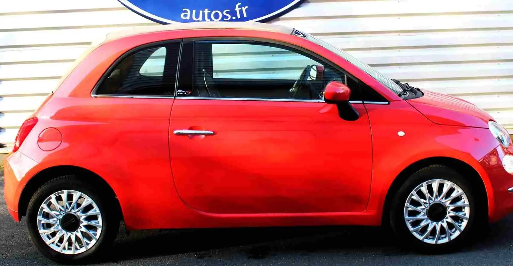 Vue de profil côté gauche d'une Fiat 500C 2018 rouge Pastel Coral avec jantes alliage et toit rigide fermé.