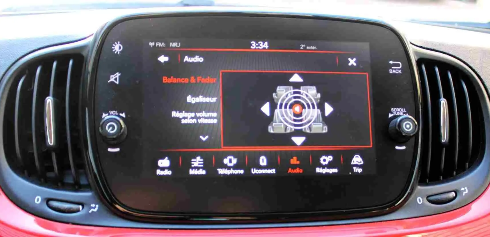 Écran tactile central de la Fiat 500C 2018 en Pastel Coral Red, affichant les réglages audio avec commandes autour.