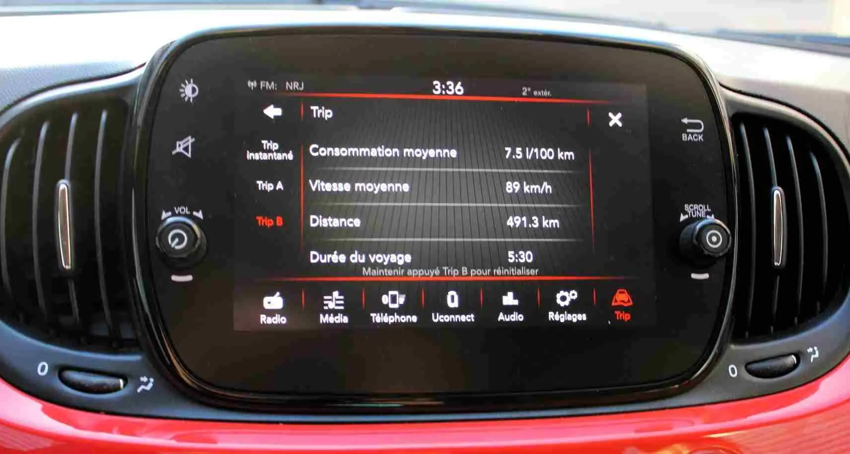 Gros plan sur l’écran tactile central du tableau de bord d’une FIAT 500C Pastel Coral Red, avec commandes autour.