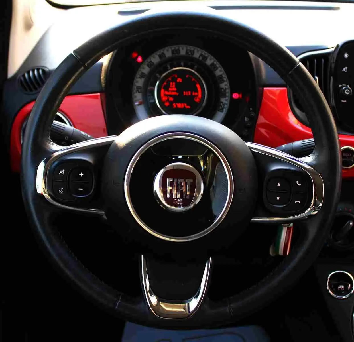 Vue intérieure centrée sur le volant noir de la Fiat 500C 2018 avec tableau de bord et inserts Pastel Coral Red.
