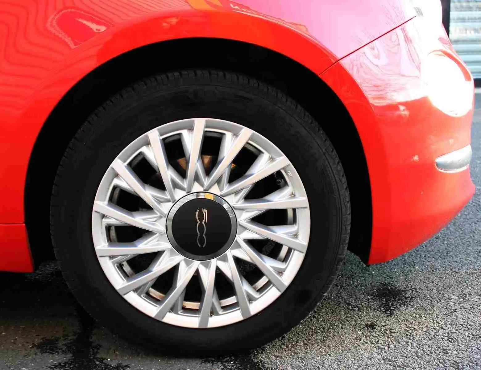 Gros plan sur la roue avant droite d'une FIAT 500C 2018 en rouge Pastel Coral avec jante argentée à rayons fins.