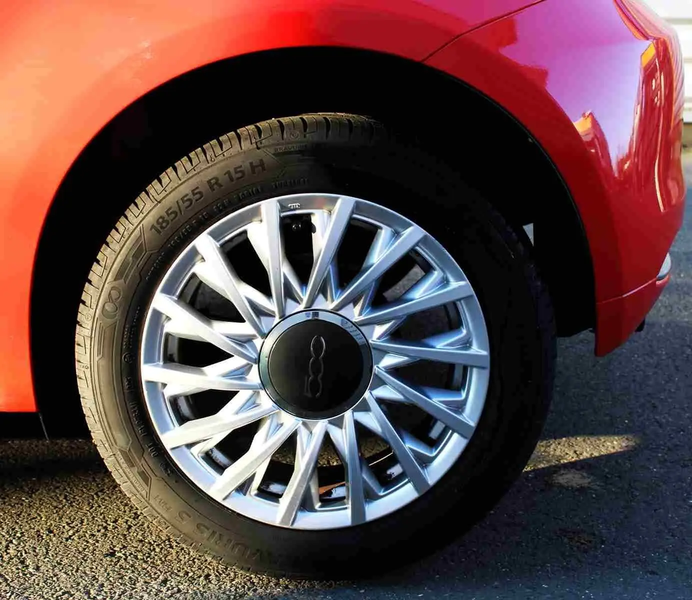 Vue 3/4 avant droite d'une Fiat 500C 2018 rouge pastel avec jantes alliage et toit ouvrant visible.