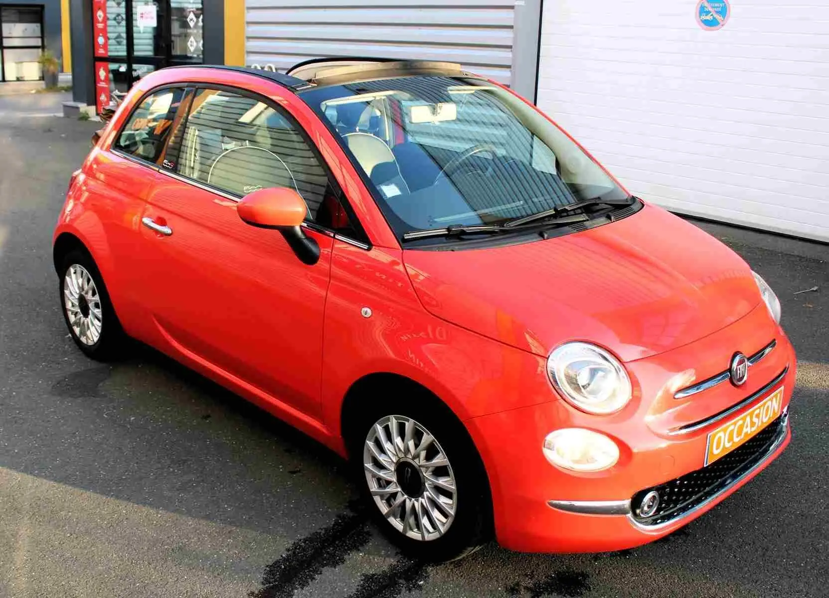 Gros plan sur la poignée intérieure chromée et les commandes de vitre côté gauche de la porte d'une Fiat 500C rouge corail.