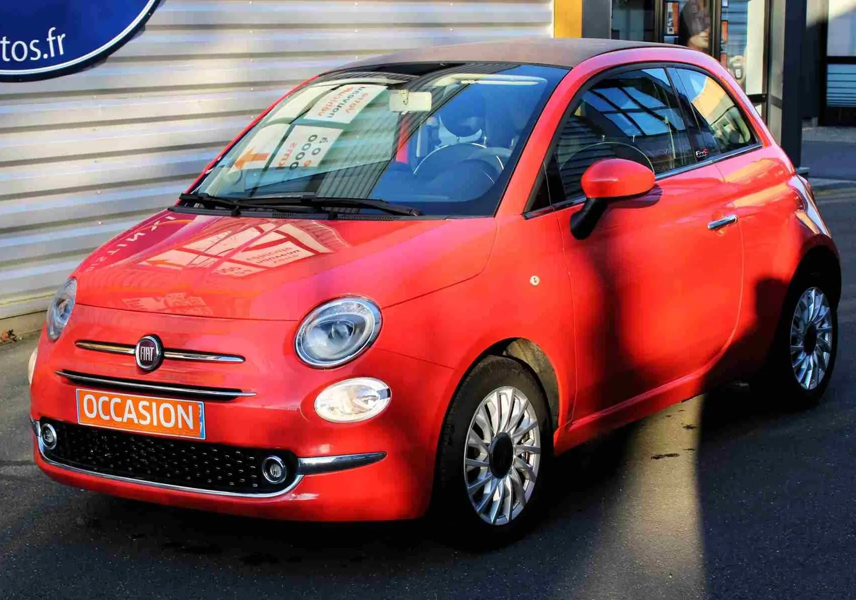 Vue 3/4 avant d'une Fiat 500C 2018 Pastel Coral Red avec toit rigide fermé et plaque "OCCASION" orange.
