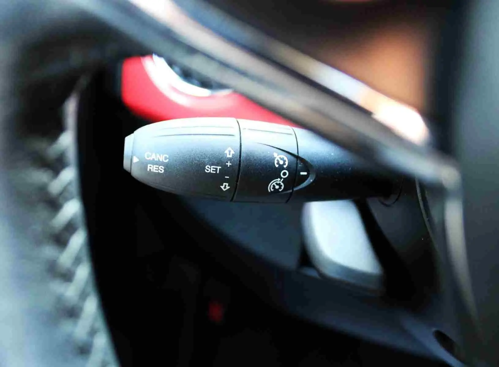 Gros plan sur la commande de régulateur de vitesse à gauche du volant d'une Fiat 500C 2018 rouge corail pastel.