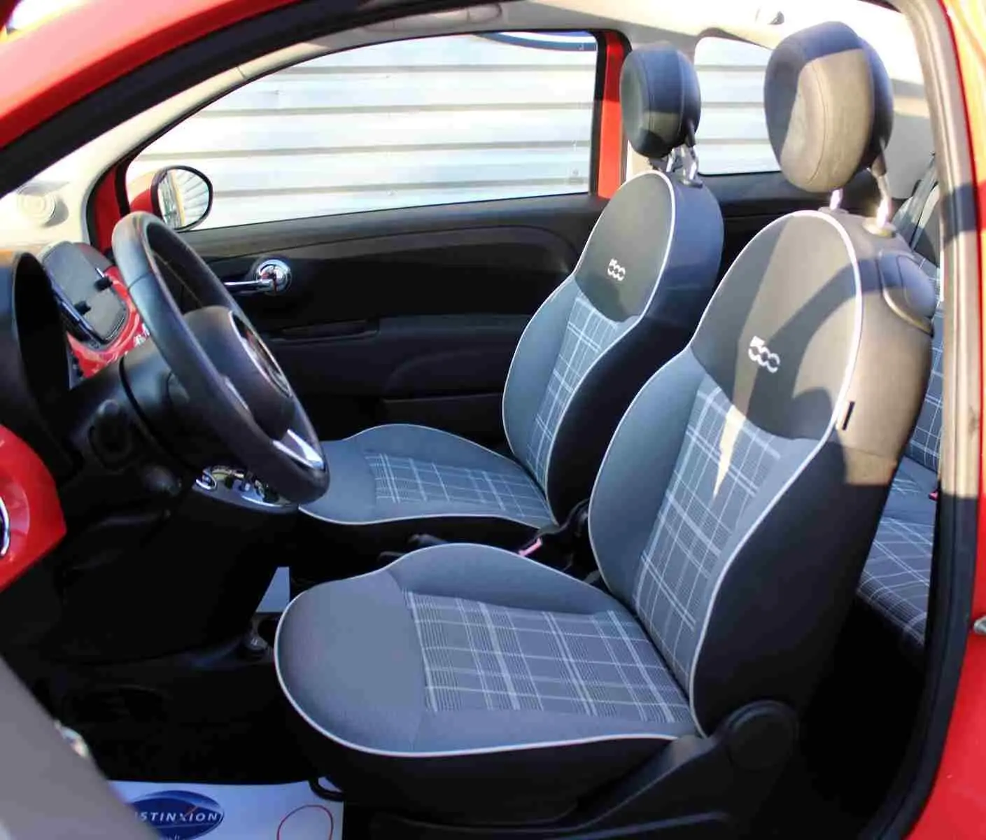 Vue intérieure côté conducteur de la FIAT 500C rouge Pastel Coral avec sièges gris à motifs et logo 500 brodé.