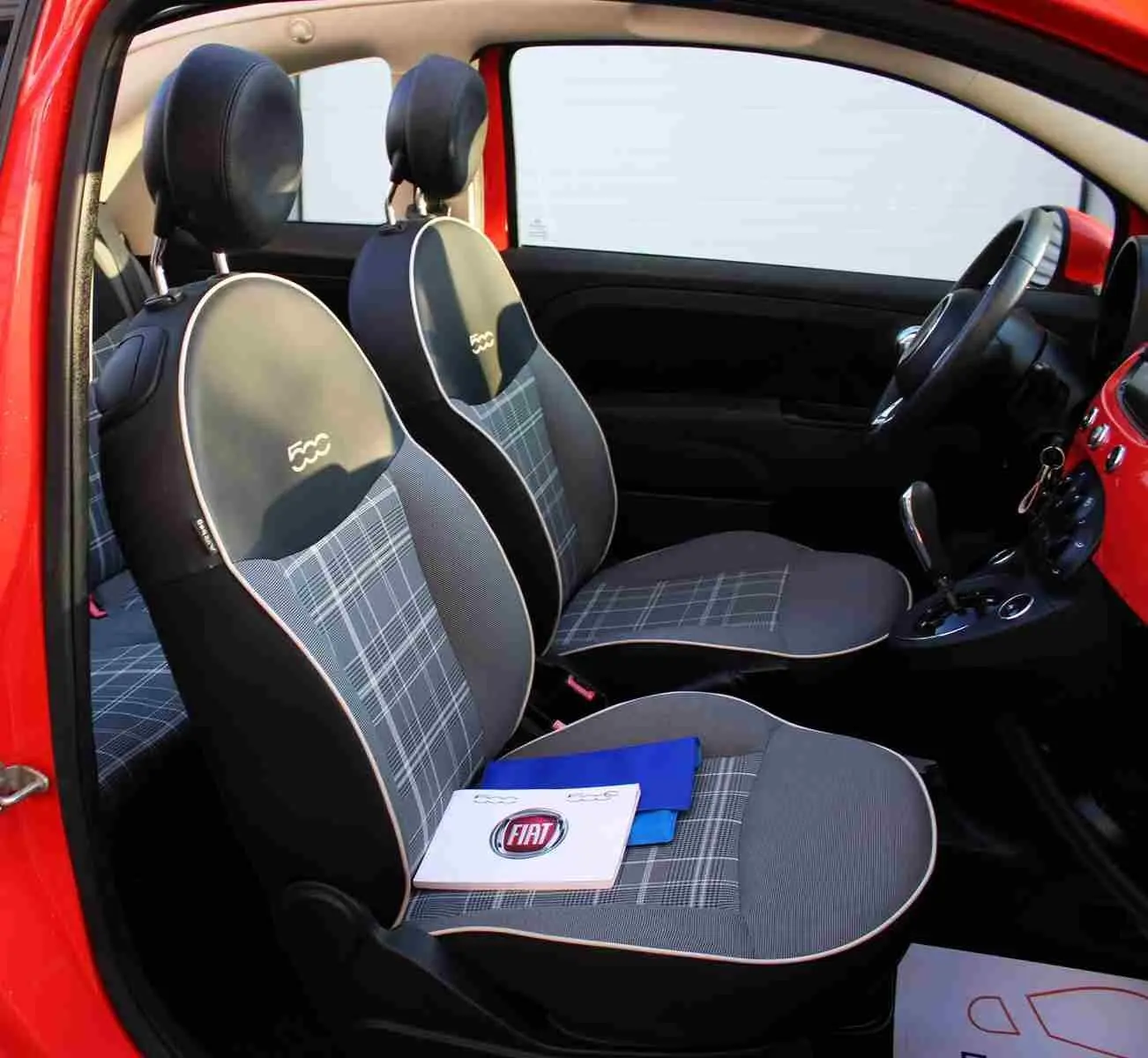 Vue intérieure côté gauche de la FIAT 500C rouge Pastel Coral avec sièges à motif écossais et logo 500 brodé.