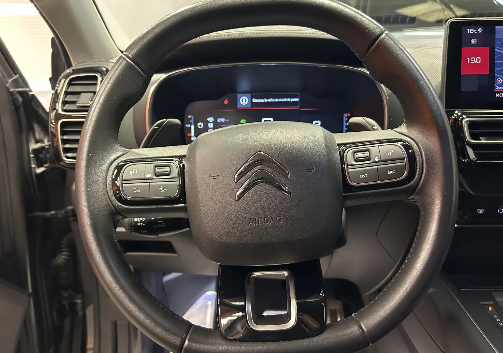 Vue rapprochée du volant cuir noir du Citroën C5 Aircross 2023 avec commandes intégrées et tableau de bord numérique.