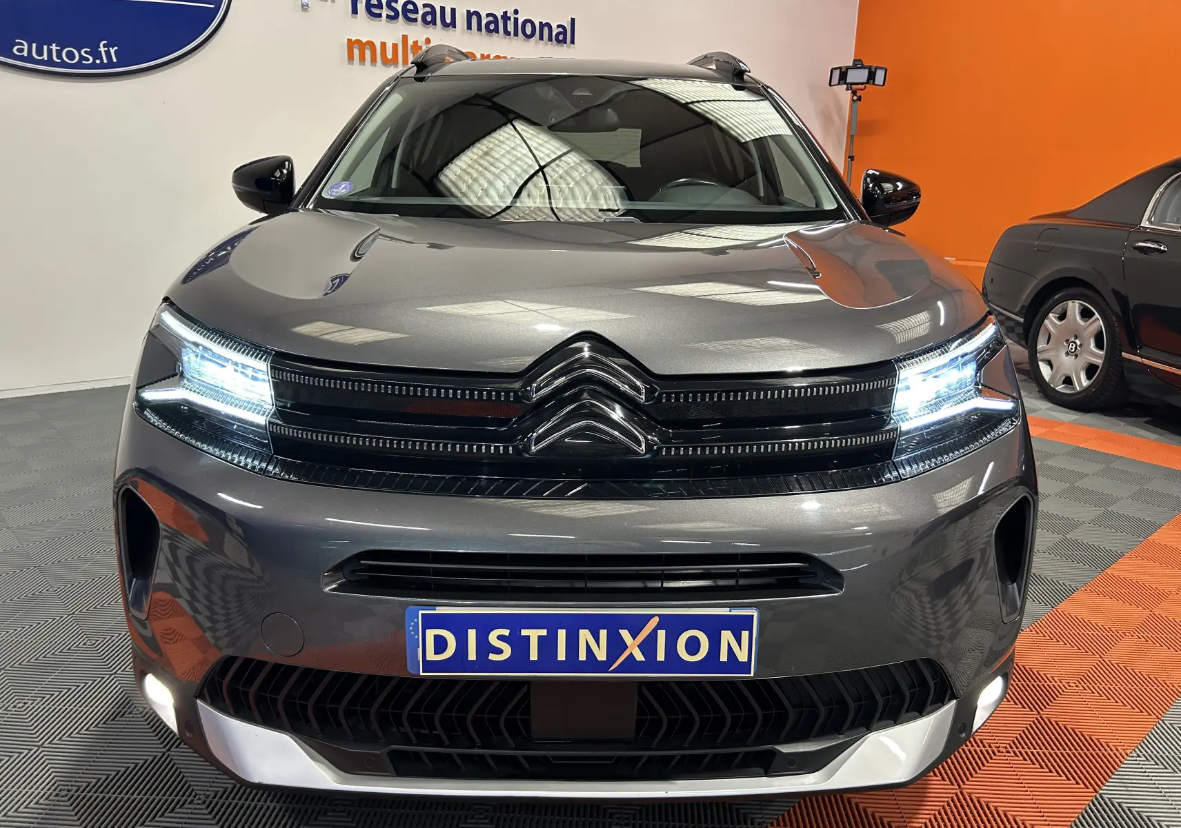 Vue de face d'un Citroën C5 Aircross gris Platinium avec phares LED allumés et plaque Distinxion visible.