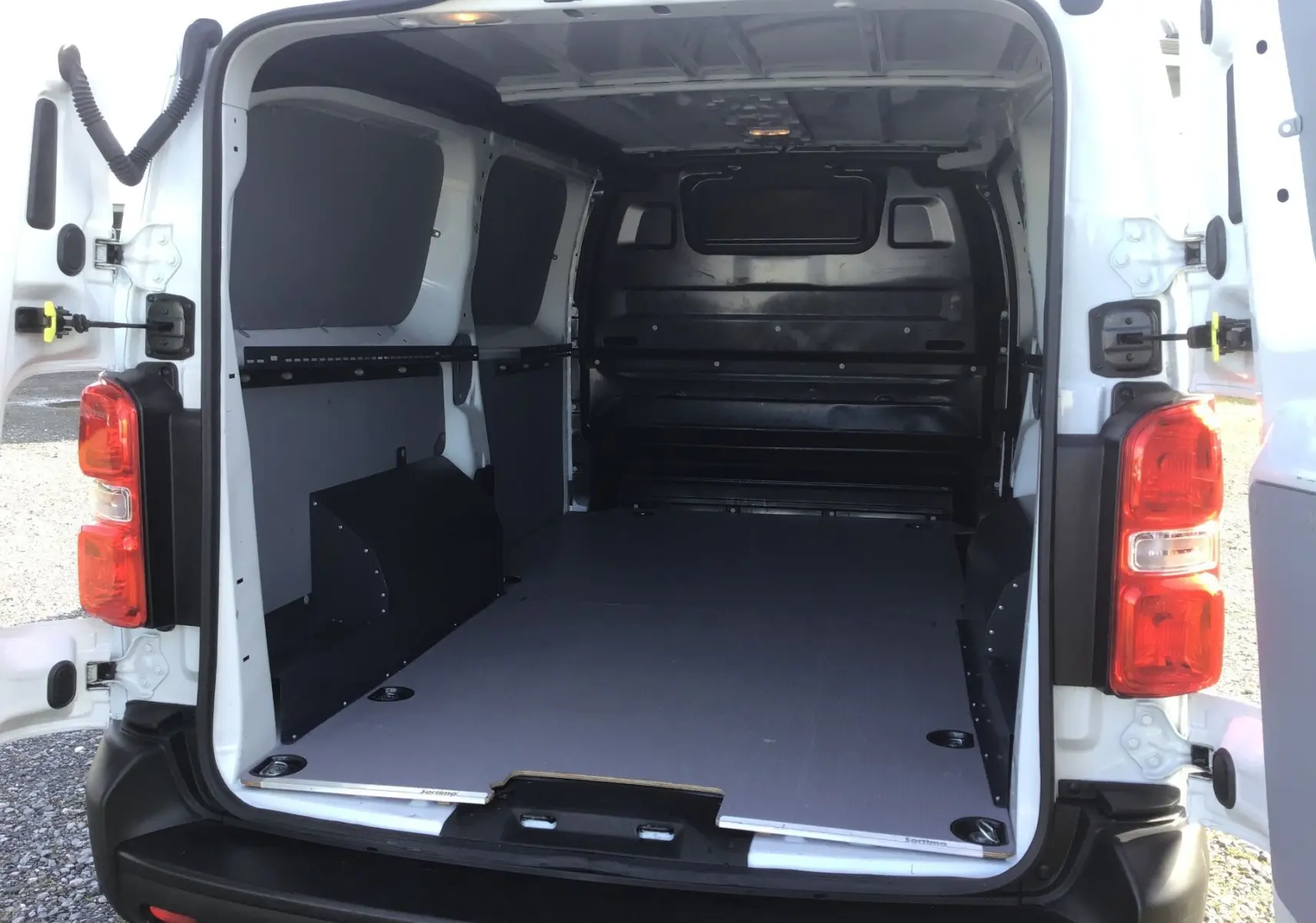 Vue arrière du fourgon blanc FIAT Scudo XL 2024, portes ouvertes montrant l’espace de chargement aménagé avec protection intérieure noire.