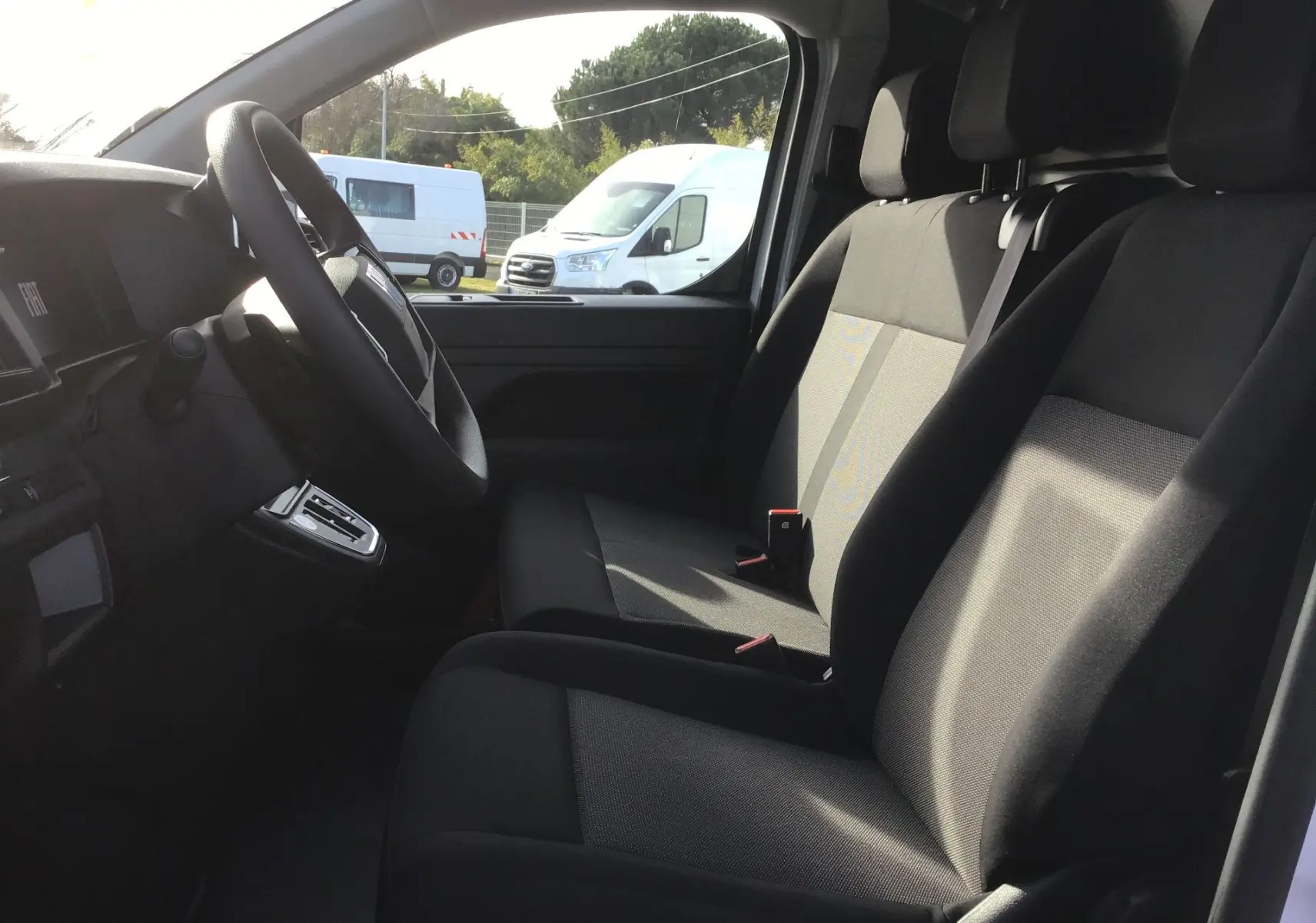 Intérieur du FIAT Scudo Fourgon blanc 2024, vue côté conducteur sur les sièges avant en tissu noir et tableau de bord.